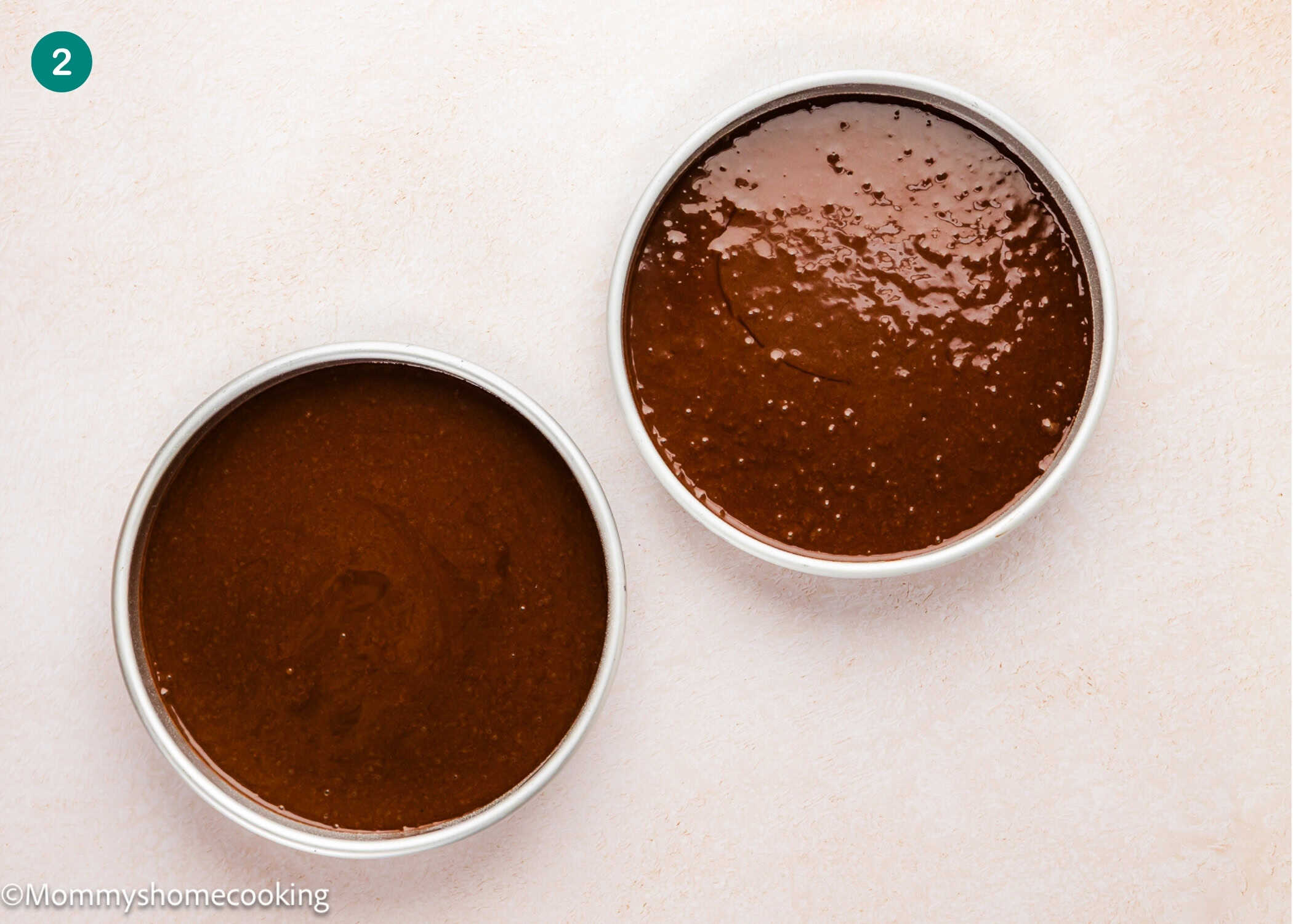Two round cake pans filled with Ultra-Fudgy Eggless Chocolate Layer Cake (Matilda Inspired) batter are placed side by side on a light-colored surface.