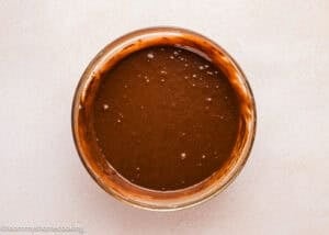 A glass bowl filled with Ultra-Fudgy Eggless Chocolate Layer Cake (Matilda Inspired) batter sits on a light-colored countertop.