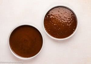 Two round cake pans filled with Ultra-Fudgy Eggless Chocolate Layer Cake (Matilda Inspired) batter are placed side by side on a light-colored surface.