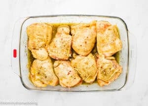 Easy Baked Lemon Chicken Thighs: Raw, seasoned chicken thighs arranged in a glass baking dish, ready for cooking on a white marble surface.