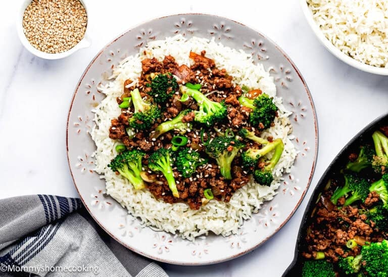 A plate of white rice topped with ground beef, broccoli, sliced green onions, and sesame seeds—an Easy Ground Beef and Broccoli (20-Minute Dinner) with extra bowls of rice and sesame seeds nearby.