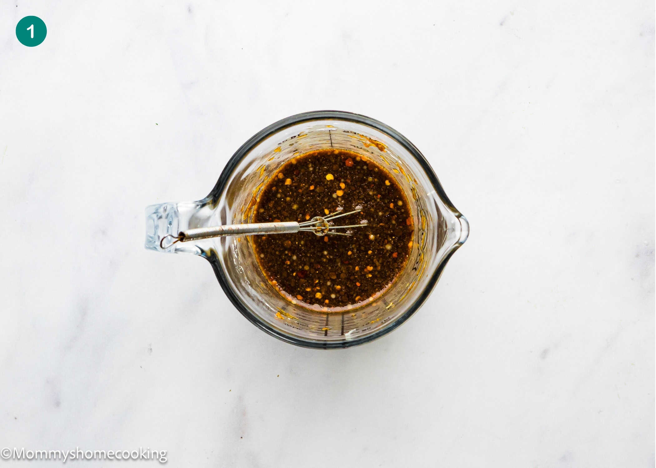 A glass measuring cup with a metal whisk contains a dark, speckled liquid mixture on a white marble surface—perfect for preparing Easy Ground Beef and Broccoli (20-Minute Dinner).