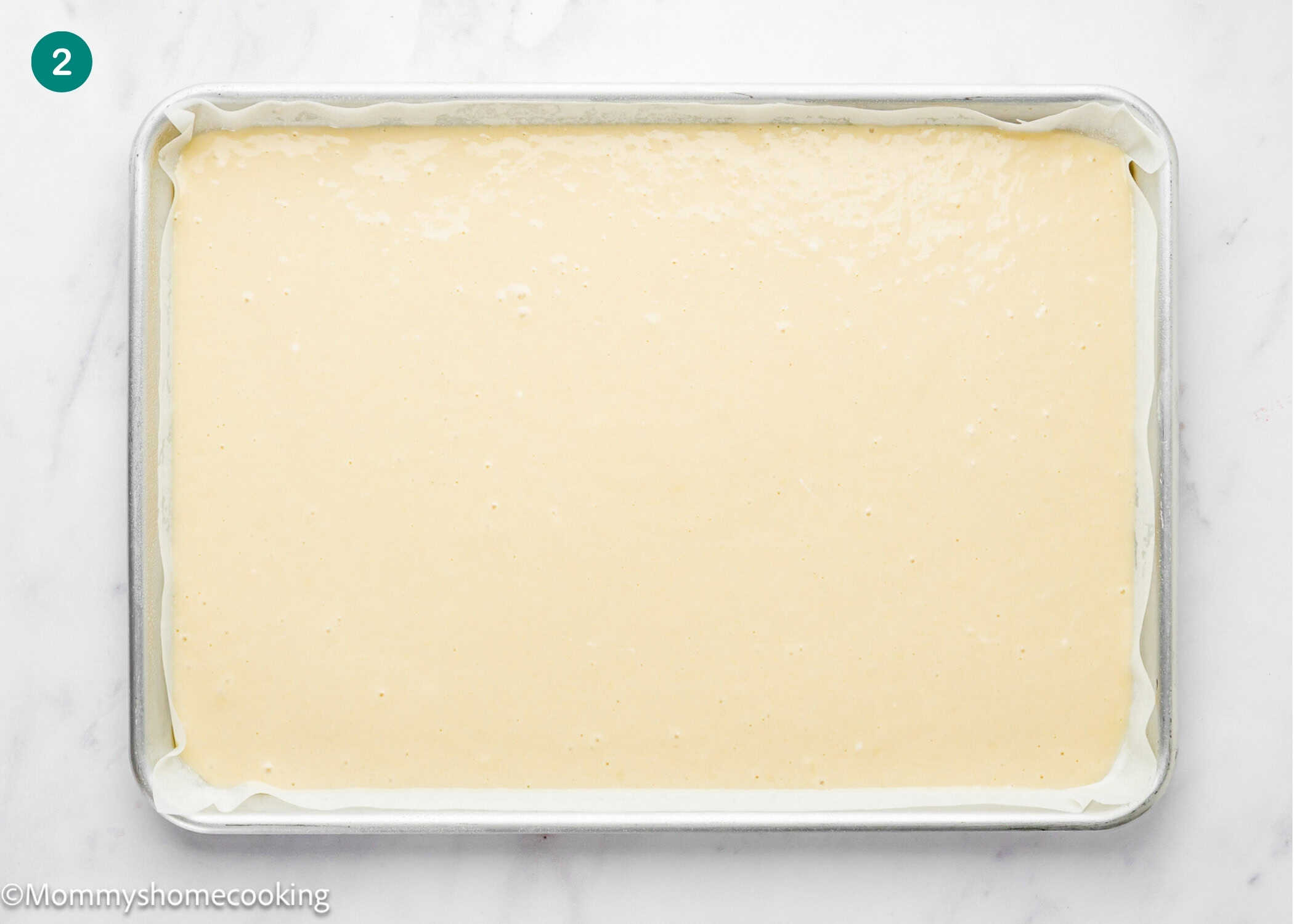 A baking sheet lined with parchment paper is filled with an even layer of Egg-Free Vanilla Roll Cake batter, ready to be baked.