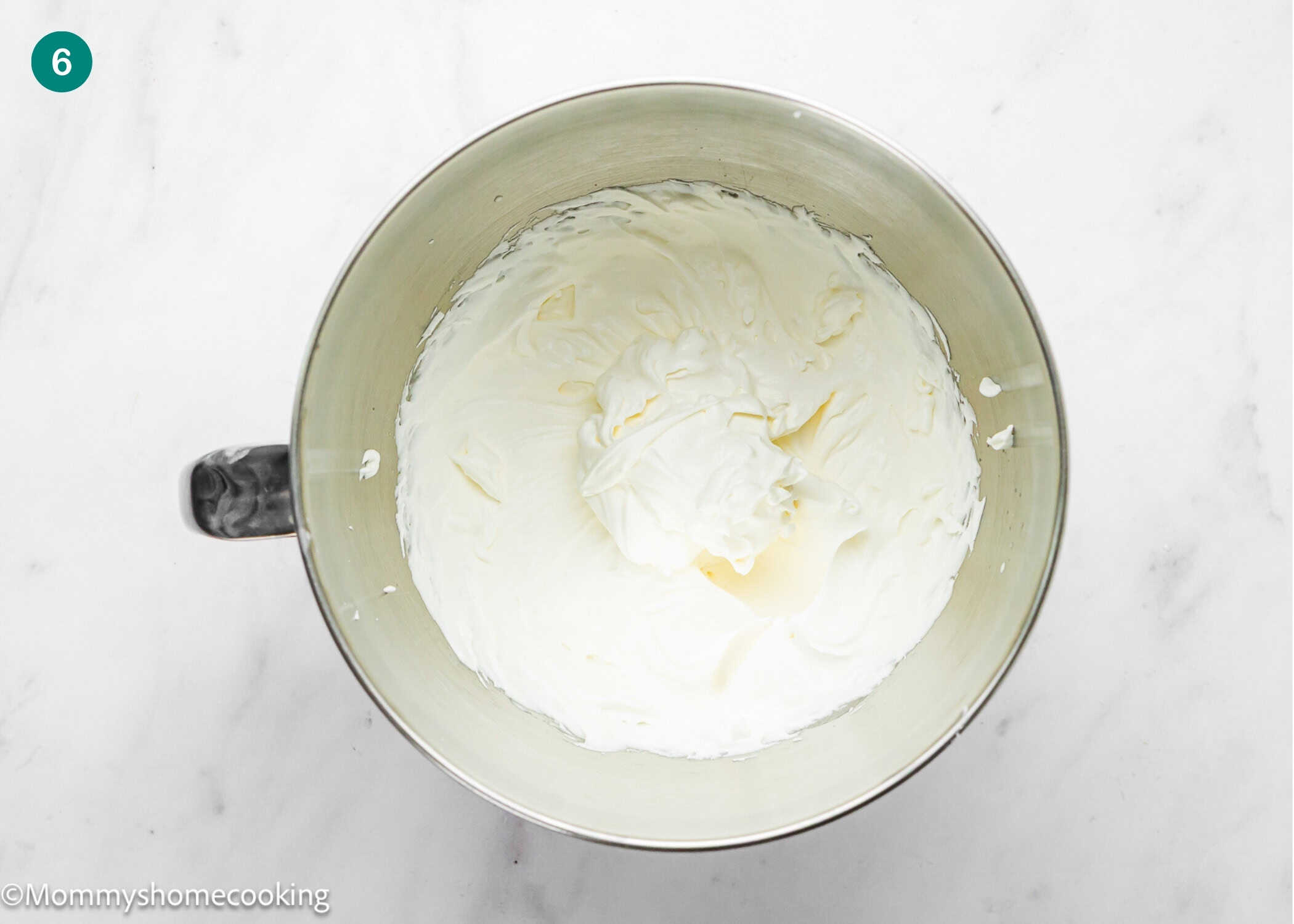 A mixing bowl filled with whipped cream cheese mixture for an Egg-Free Vanilla Roll Cake sits on a white marble surface.