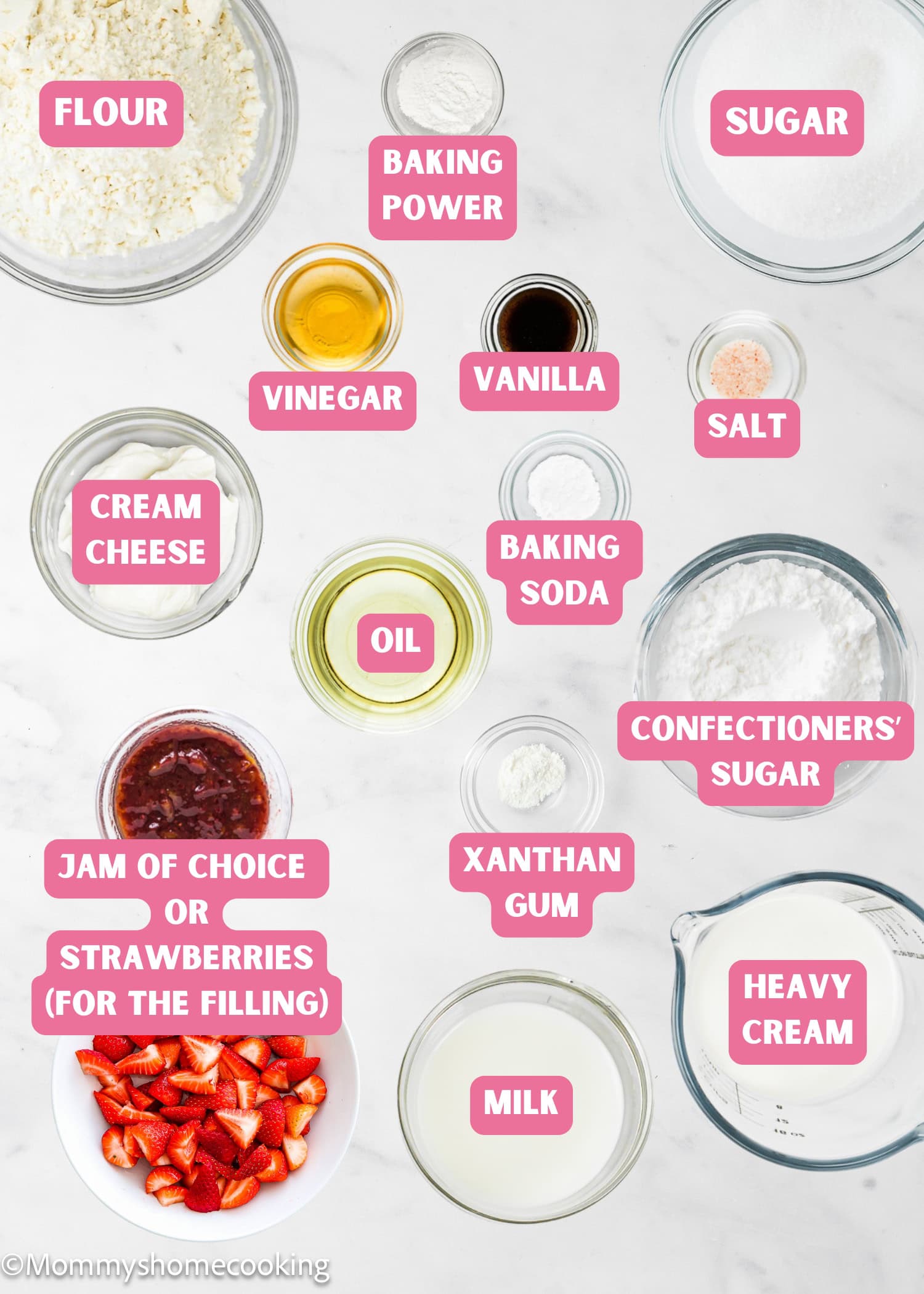 Ingredients for an Egg-Free Vanilla Roll Cake are arranged on a white surface, including flour, sugar, baking powder, vinegar, vanilla, salt, cream cheese, oil, baking soda, confectioners’ sugar, xanthan gum, milk, heavy cream, and fruit jam or strawberries.