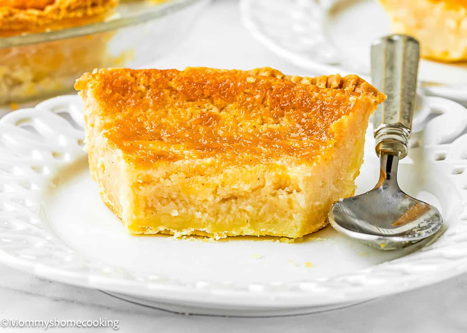 A slice of Eggless Buttermilk Pie on a white plate with a silver spoon beside it.