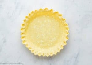 An empty, unbaked pie crust with crimped edges sits in a pie dish on a light marble surface, ready for a delicious Eggless Buttermilk Pie.