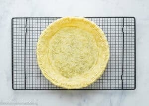 An Eggless Buttermilk Pie crust sits on a cooling rack, viewed from above on a white marble surface.