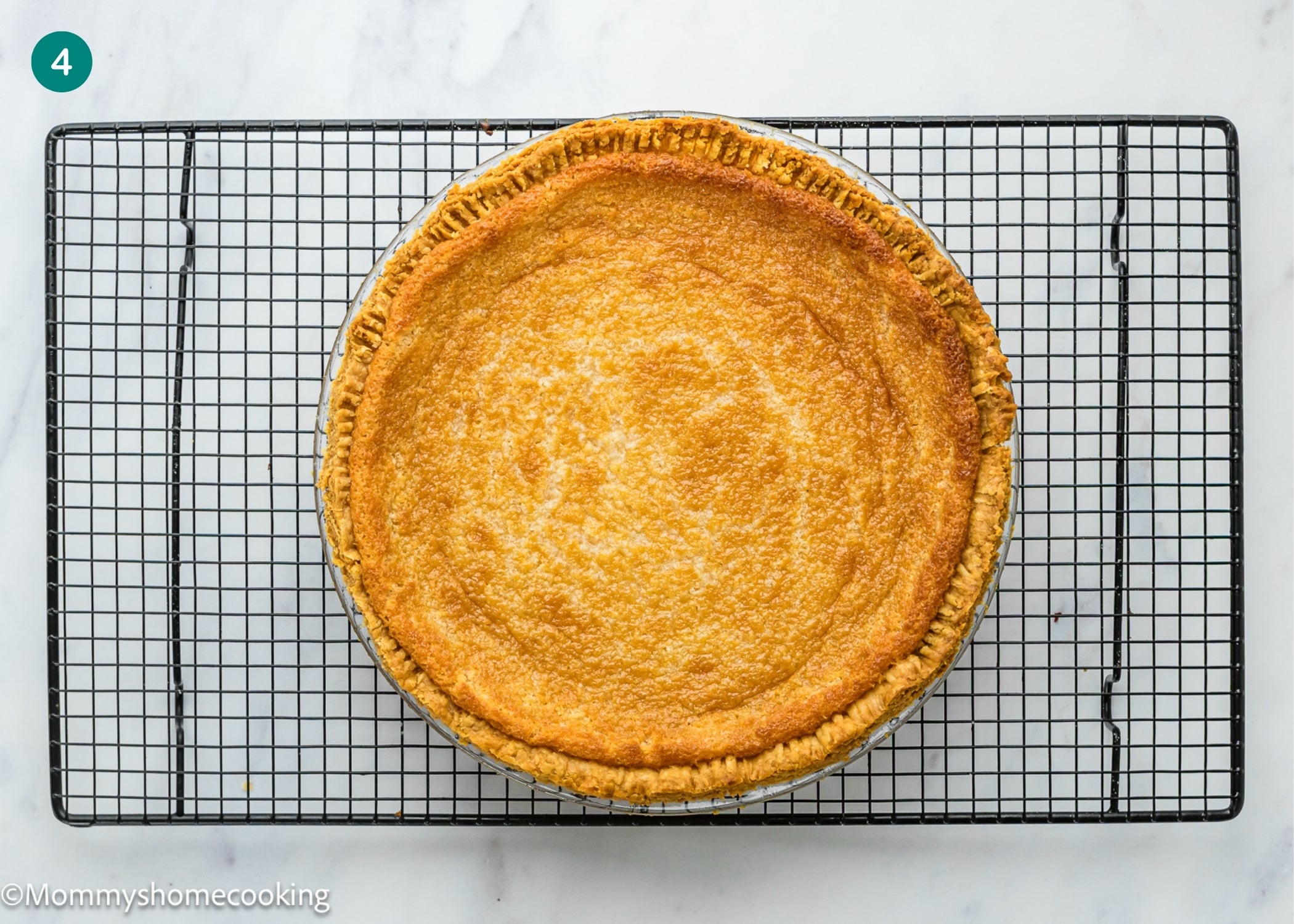 An Eggless Buttermilk Pie with a golden brown crust cools on a black wire rack over a white marble surface.