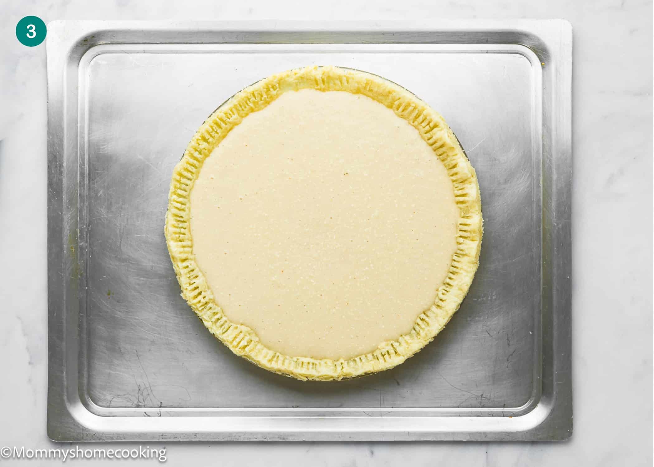 Eggless Buttermilk Pie with fork-pressed edges sits unbaked on a metal baking sheet, viewed from above on a white surface.