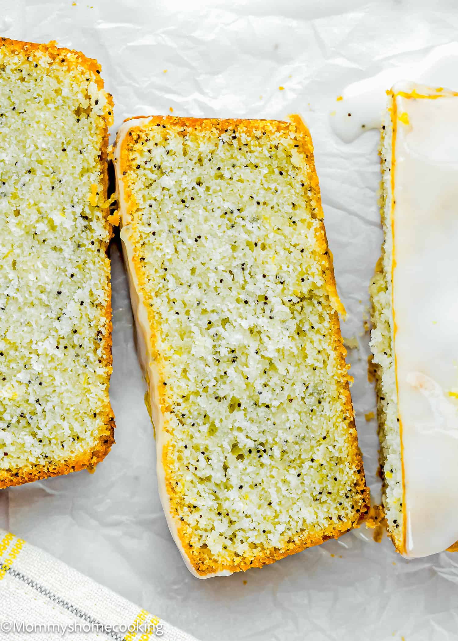 Close-up of three slices of Eggless Lemon Poppy Seed Loaf Cake with a light glaze on top, displayed on white parchment paper.