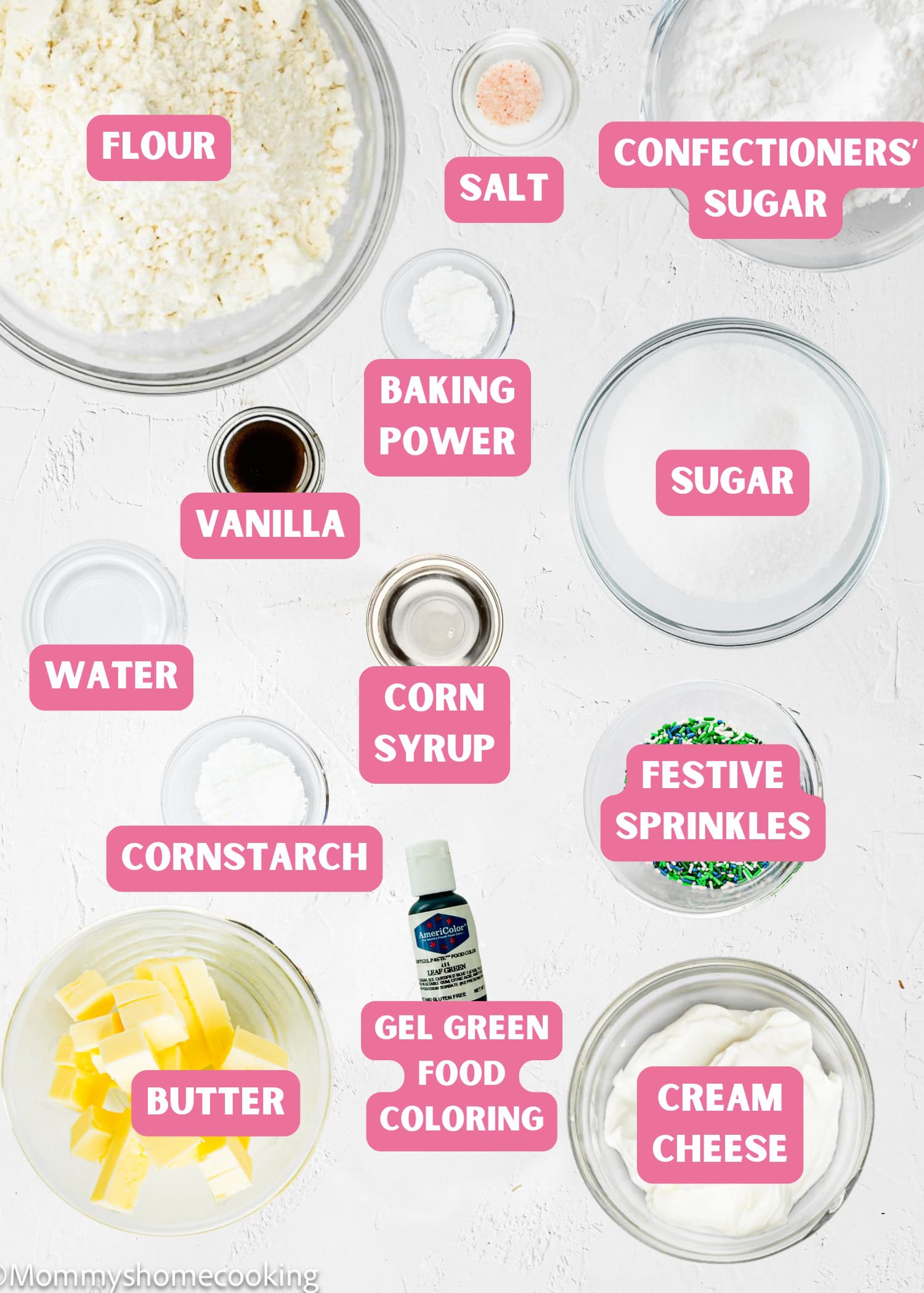 Various baking ingredients in clear bowls are labeled: flour, salt, confectioners’ sugar, baking powder, sugar, vanilla, corn syrup, festive sprinkles, water, butter, gel green food coloring, and cream cheese—perfect for Eggless Patrick’s Day Sugar Cookies.