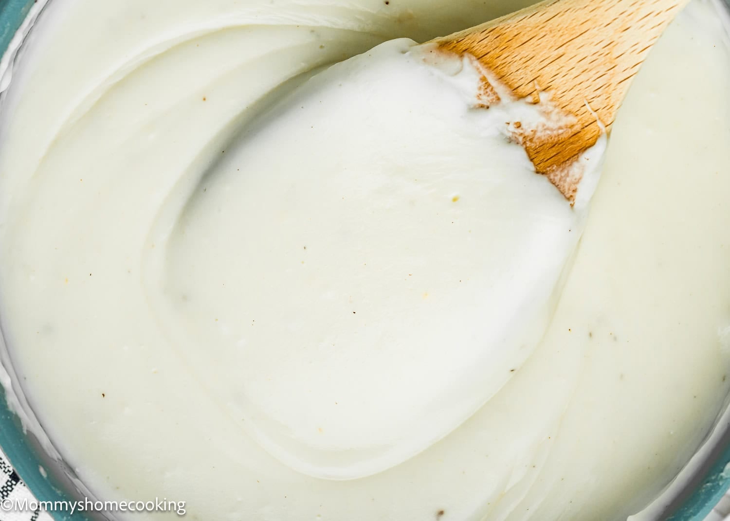 Close-up of a wooden spoon stirring thick, creamy Easy Béchamel Sauce (Classic White Sauce Recipe) in a bowl.