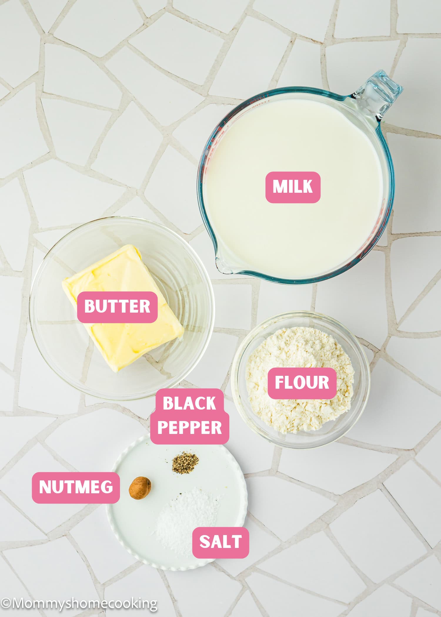 Overhead view of labeled ingredients for Easy Béchamel Sauce (Classic White Sauce Recipe): milk, butter, flour, black pepper, nutmeg, and salt arranged on a white tiled surface.
