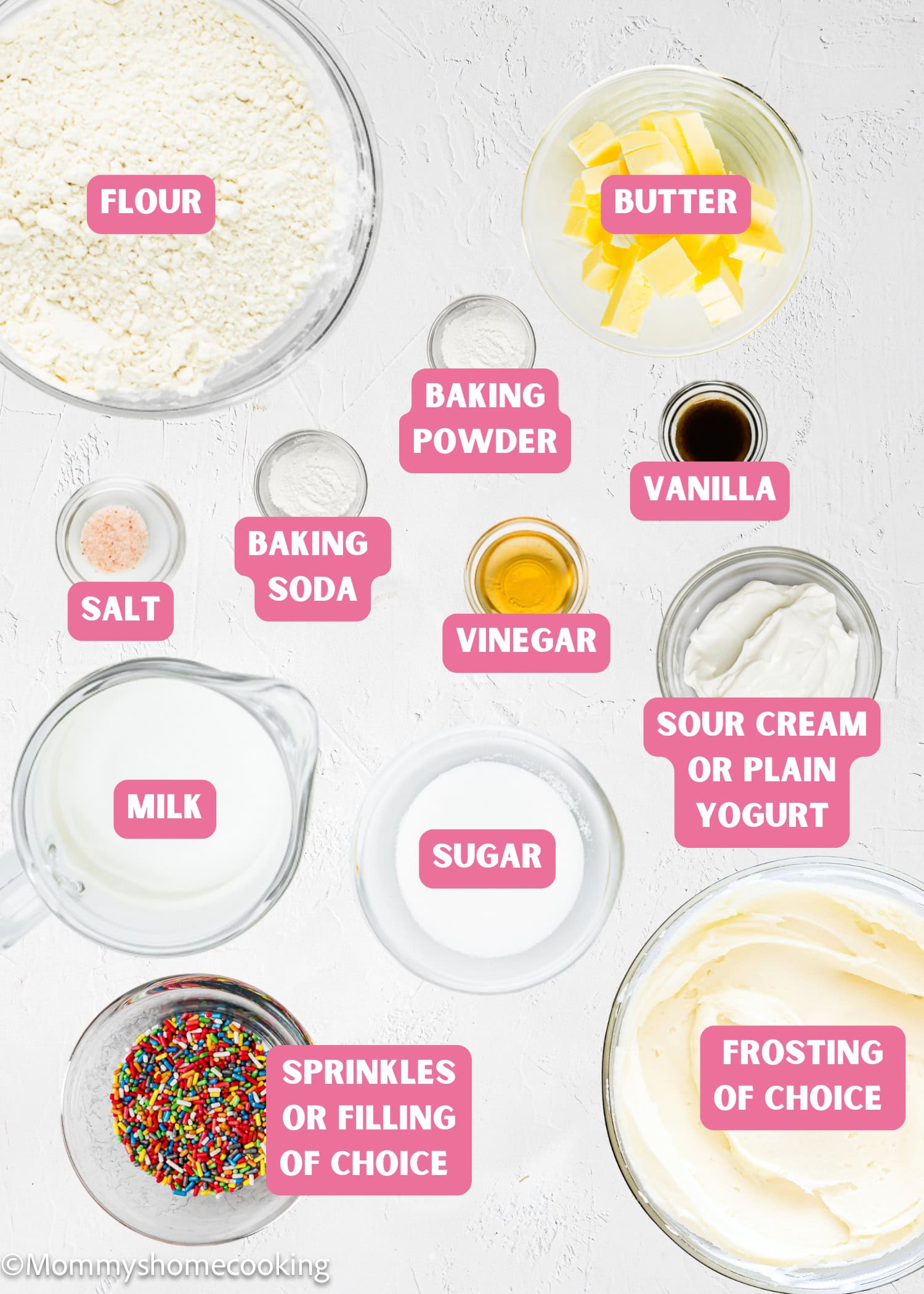 Top-down view of labeled baking ingredients in bowls and cups for Eggless Birthday Cupcakes (With Surprise Inside): flour, butter, baking powder, salt, vanilla, vinegar, yogurt or sour cream, milk, sugar, sprinkles, frosting.