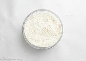 A glass bowl filled with white flour mixture sits on a white surface, ready to make Eggless Birthday Cupcakes (With Surprise inside).