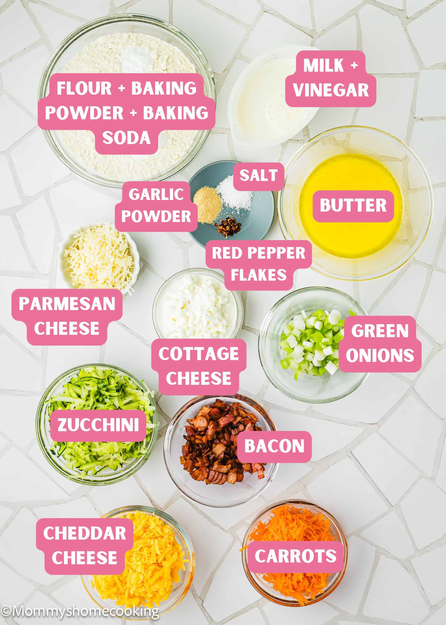 Top-down view of labeled ingredients for Eggless Cheesy Savory Muffins in bowls—flour mixture, cheeses, vegetables, seasonings, melted butter, milk with vinegar, and cooked bacon—arranged on a white tiled surface.