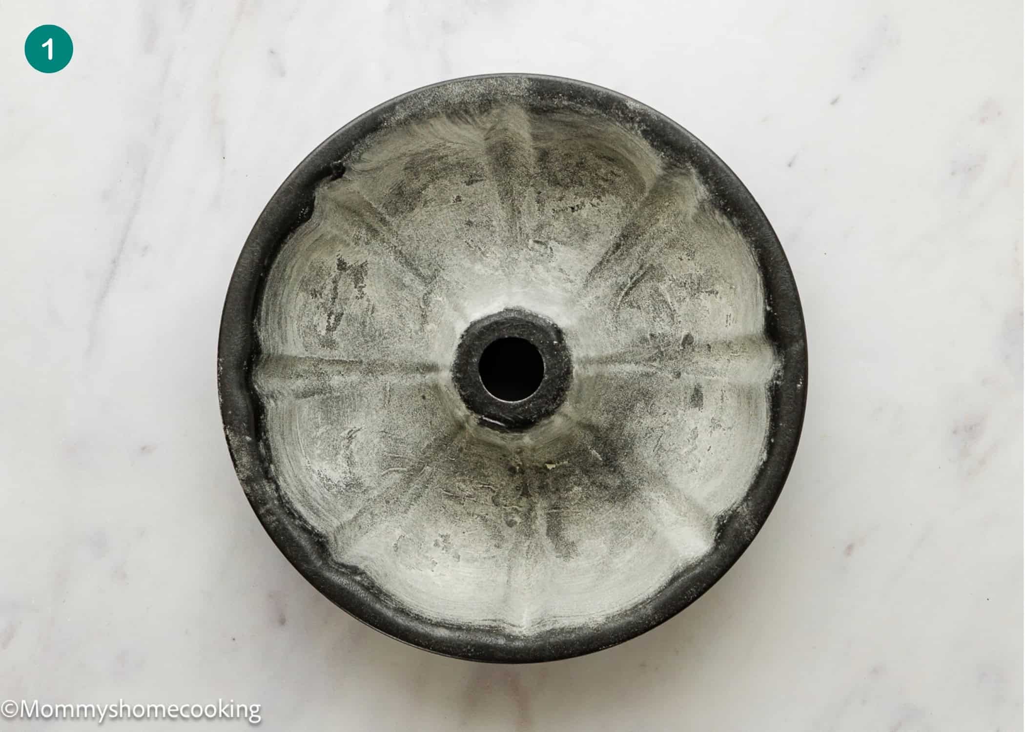 An Eggless Coconut Bundt Cake pan sits greased and floured on a white marble surface, viewed from above.