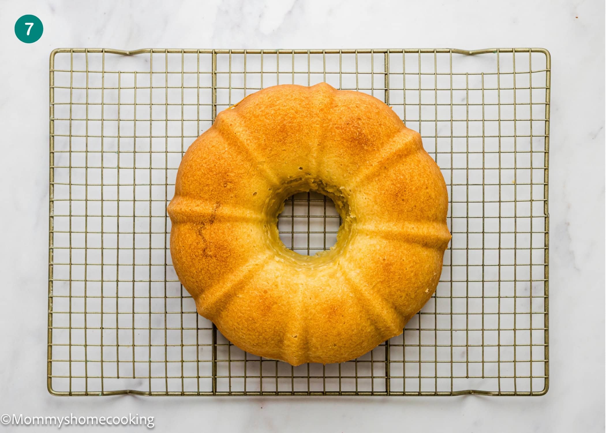 An Eggless Coconut Bundt Cake sits on a cooling rack atop a white marble surface.