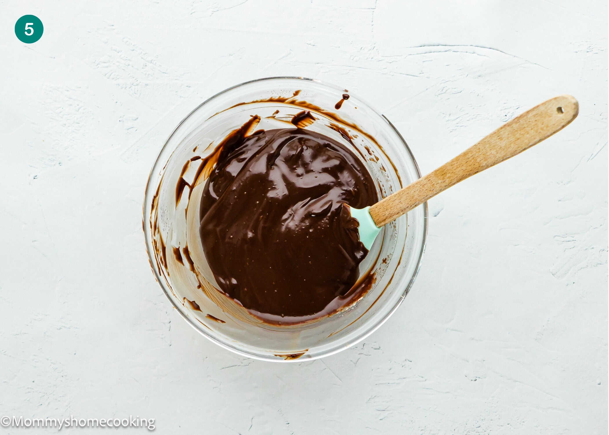 A glass bowl filled with melted chocolate and a spatula rests on a white surface, ready for making Eggless Cosmic Brownies.