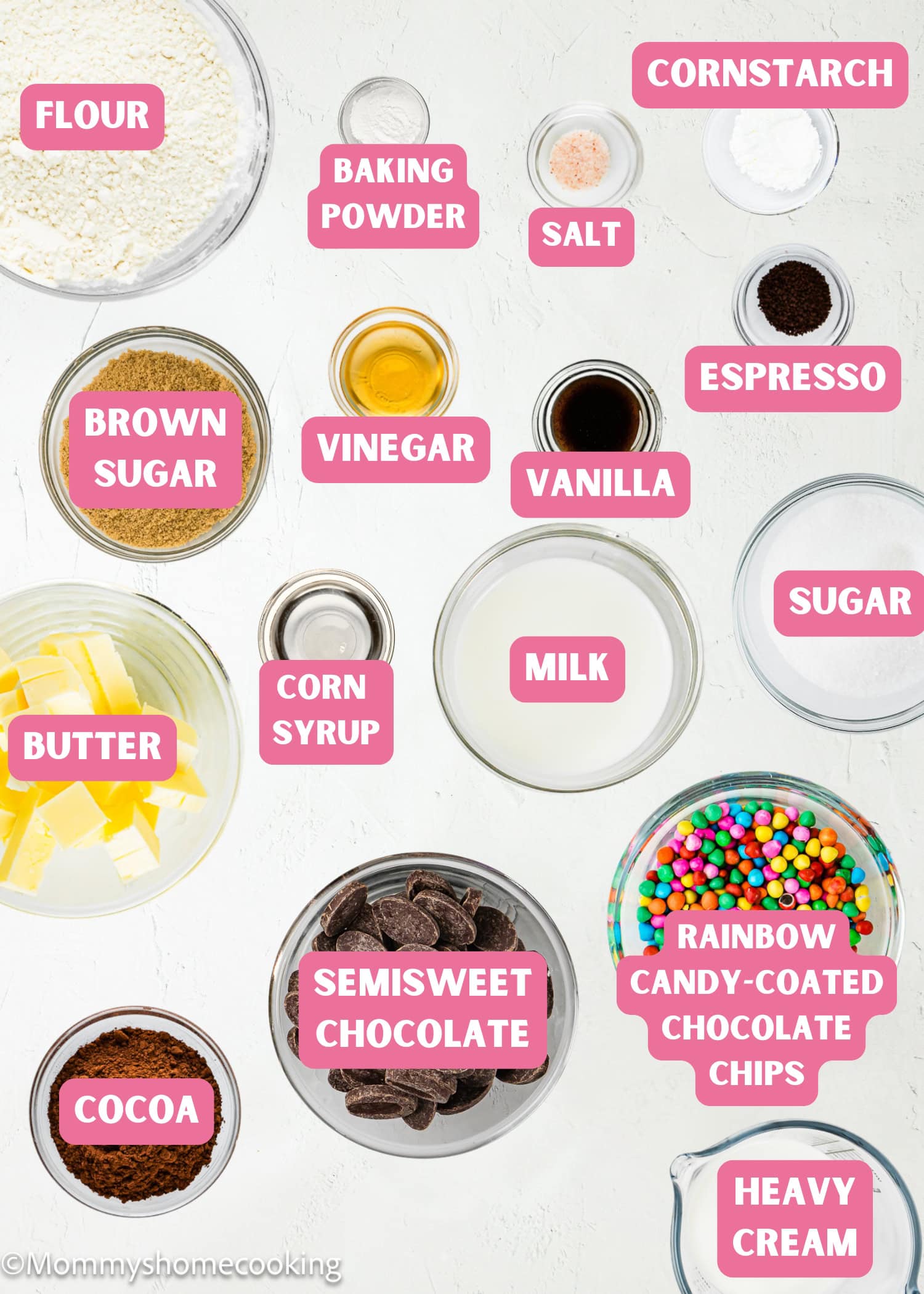 An assortment of labeled baking ingredients in bowls for Eggless Cosmic Brownies, including flour, brown sugar, cocoa, butter, milk, cornstarch, heavy cream, chocolate, vanilla, and candy-coated chips.