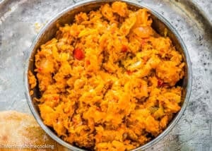 A metal bowl filled with shredded, cooked yellow and orange vegetables, including peppers and onions, on a silver tray—perfect as a filling for Venezuelan Cazón Empanadas.