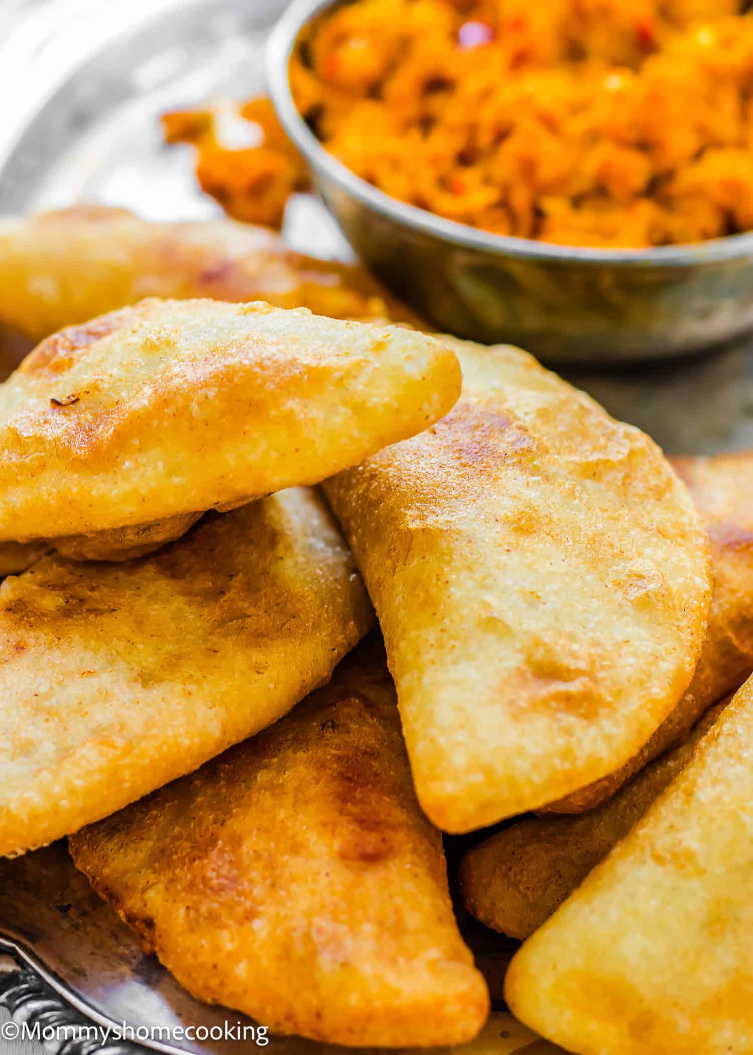 A plate of golden-brown Venezuelan Cazón Empanadas is served with a side of shredded vegetable salad in a metal bowl.