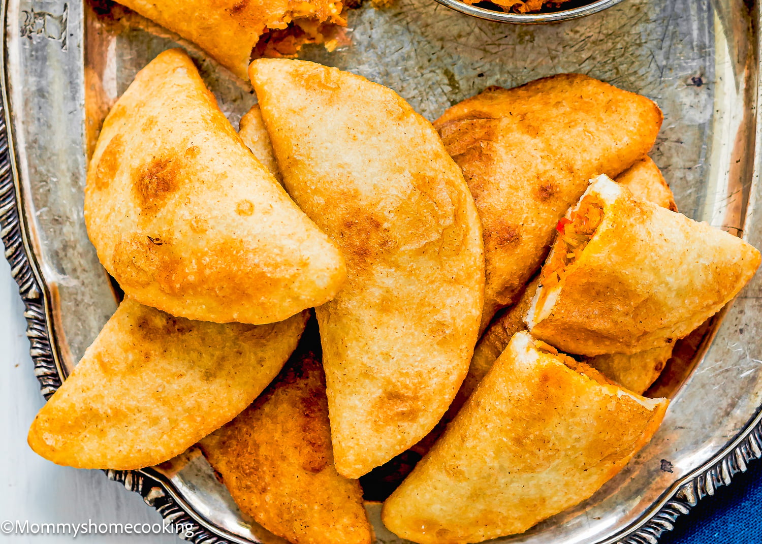 A close-up of several Venezuelan Cazón Empanadas on a silver tray, with one empanada cut open to show its savory filling.