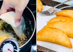 A hand places a raw Venezuelan Cazón Empanada into hot oil to fry, while golden-brown empanadas cool on a tray lined with paper towels.