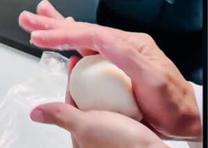 Hands shaping a ball of dough on a white surface, preparing Venezuelan Cazón Empanadas.