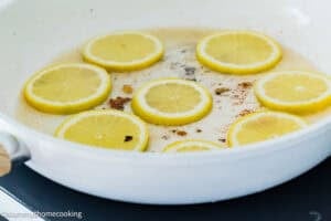 Sliced lemons cooking in a white skillet with browned bits and light residue, perfect for preparing Eggless Chicken Francese (Chicken French).