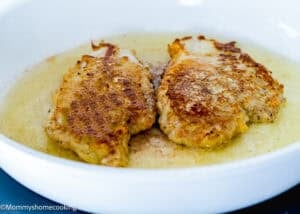 Two breaded chicken cutlets frying in oil in a white skillet, perfect for preparing Eggless Chicken Francese (Chicken French).