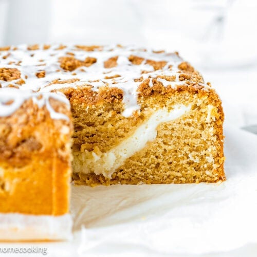 A sliced Eggless Cream Cheese Coffee Cake with crumb topping and icing, revealing a layer of creamy filling inside.