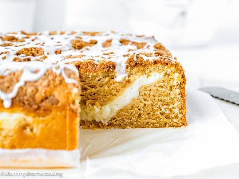 A sliced Eggless Cream Cheese Coffee Cake with crumb topping and icing, revealing a layer of creamy filling inside.
