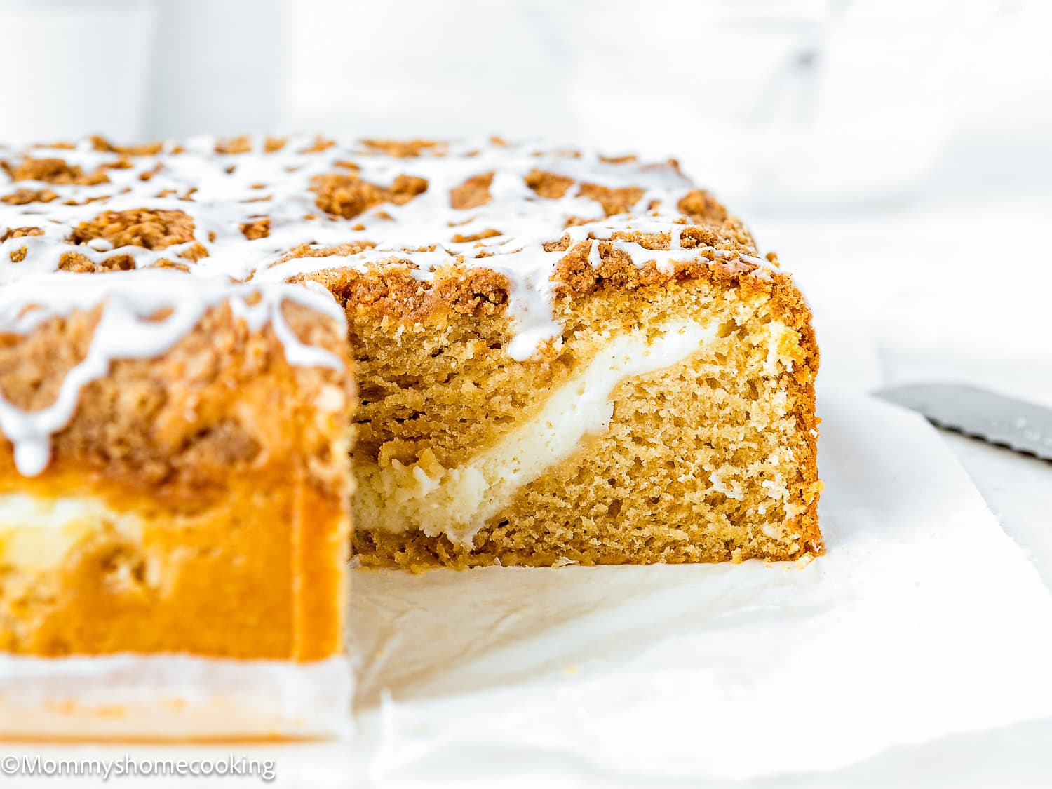 A sliced Eggless Cream Cheese Coffee Cake with crumb topping and icing, revealing a layer of creamy filling inside.