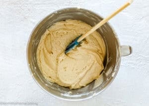 A metal mixing bowl filled with smooth, light-colored dough for Eggless Cream Cheese Coffee Cake and a blue spatula resting inside.