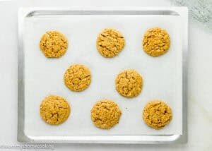 Eight Eggless Peanut Butter Oatmeal Cookies on a parchment-lined baking sheet, arranged in rows, fresh from the oven.