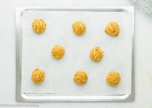 Nine evenly spaced scoops of Eggless Peanut Butter Oatmeal Cookie dough are placed on a parchment-lined baking sheet, ready to be baked.