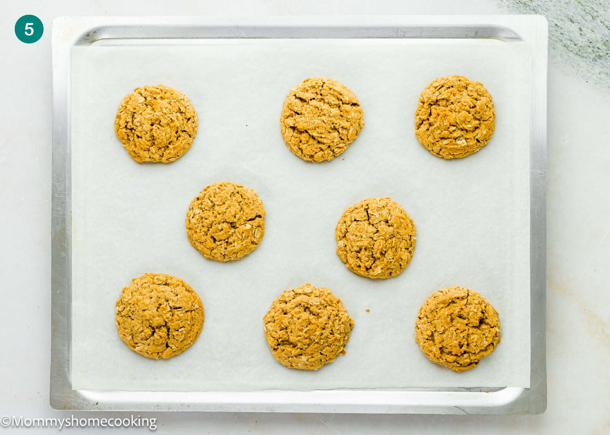 Eight Eggless Peanut Butter Oatmeal Cookies are arranged in three rows on a parchment-lined baking sheet.