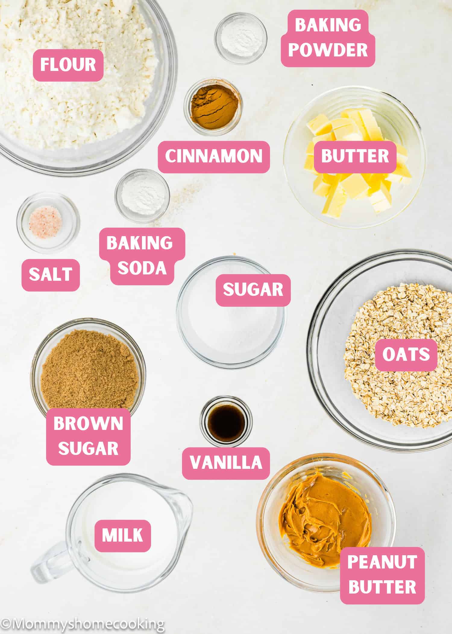 Bowls and containers with labeled ingredients for baking Eggless Peanut Butter Oatmeal Cookies, including flour, baking powder, cinnamon, butter, salt, baking soda, sugar, oats, brown sugar, vanilla, milk, and peanut butter.