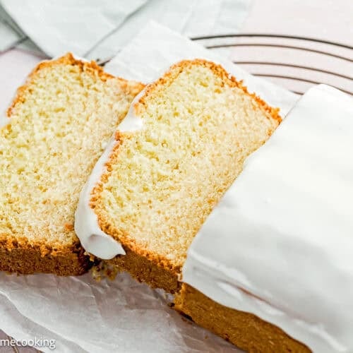 An Eggless Pound Cake Loaf sits on parchment paper on a cooling rack, with two slices cut and placed next to it.