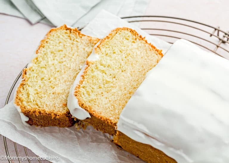 An Eggless Pound Cake Loaf sits on parchment paper on a cooling rack, with two slices cut and placed next to it.