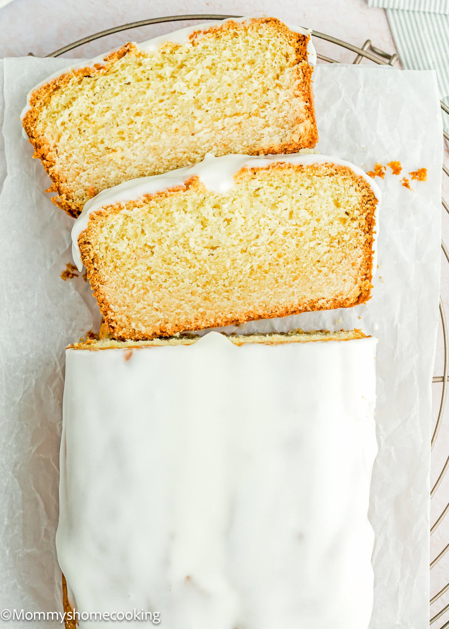 An Eggless Pound Cake Loaf sits on parchment paper, with two slices cut and neatly placed on top.