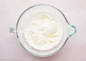 A glass mixing bowl containing whipped cream and a dollop of unincorporated cream sits on a light-colored surface, perfect for pairing with an Eggless Pound Cake Loaf.