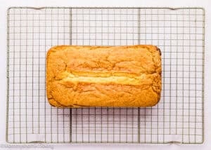 An Eggless Pound Cake Loaf, golden brown and freshly baked, cools on a wire rack against a light background.