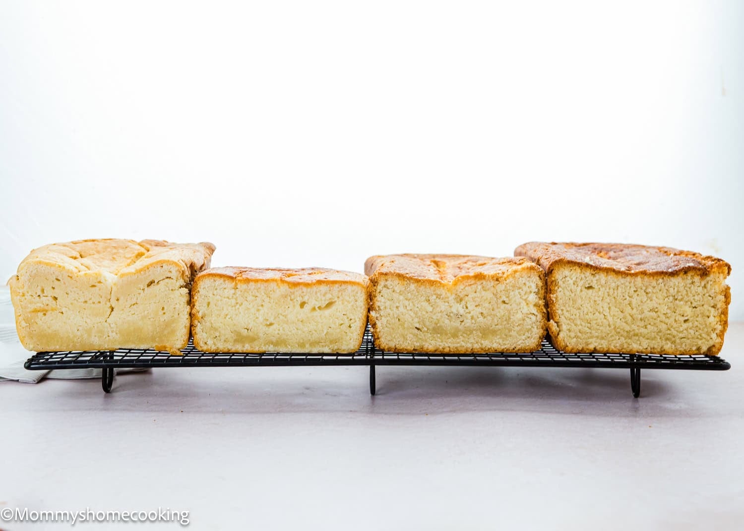 Four loaves, including an Eggless Pound Cake Loaf, are cooling on a wire rack, each with a slightly different shape and crust color, against a plain white background.