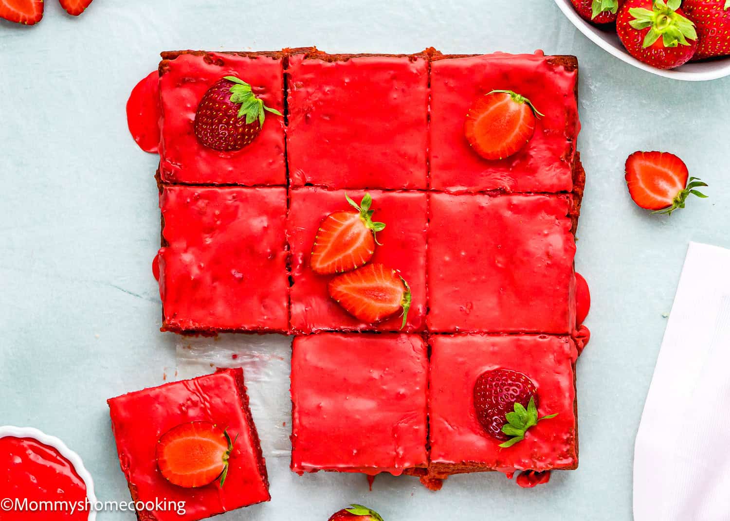 Nine Eggless Strawberry Brownies, each topped with a halved strawberry, arranged on a light surface with extra strawberries around.