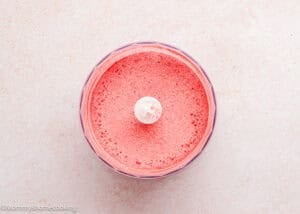 A food processor bowl filled with finely ground pink powder, viewed from above on a light-colored surface—perfect for making Eggless Strawberry Brownies.
