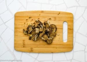 Sliced and crumbled pieces of brown bread on a wooden cutting board placed on a white tiled surface, next to a glass of Papelón con Limón (Venezuelan Limeade).