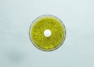 A food processor bowl filled with grinded pistachios sits on a light blue surface, viewed from above.
